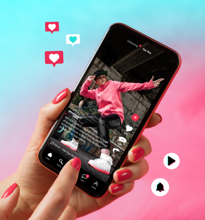 Feminine hands with pink nail polish holding a smartphone displaying an influencer's TikTok profile, surrounded by floating hearts and play button icons, advertising a SkillsFuture eligible TikTok marketing course in Singapore that teaches essential TikTok editing skills and techniques.