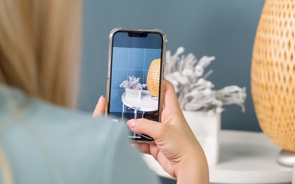 A woman practises her digital photography skills with a smartphone using the rule of thirds, focusing on a vase of flowers and a woven basket in the background.