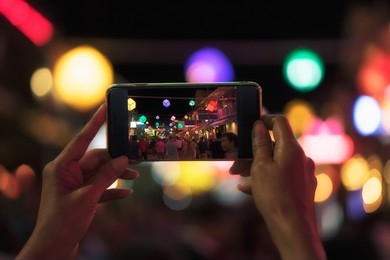 A creative depiction of fine art photography with hands holding a smartphone that digitally frames a bustling night market scene.