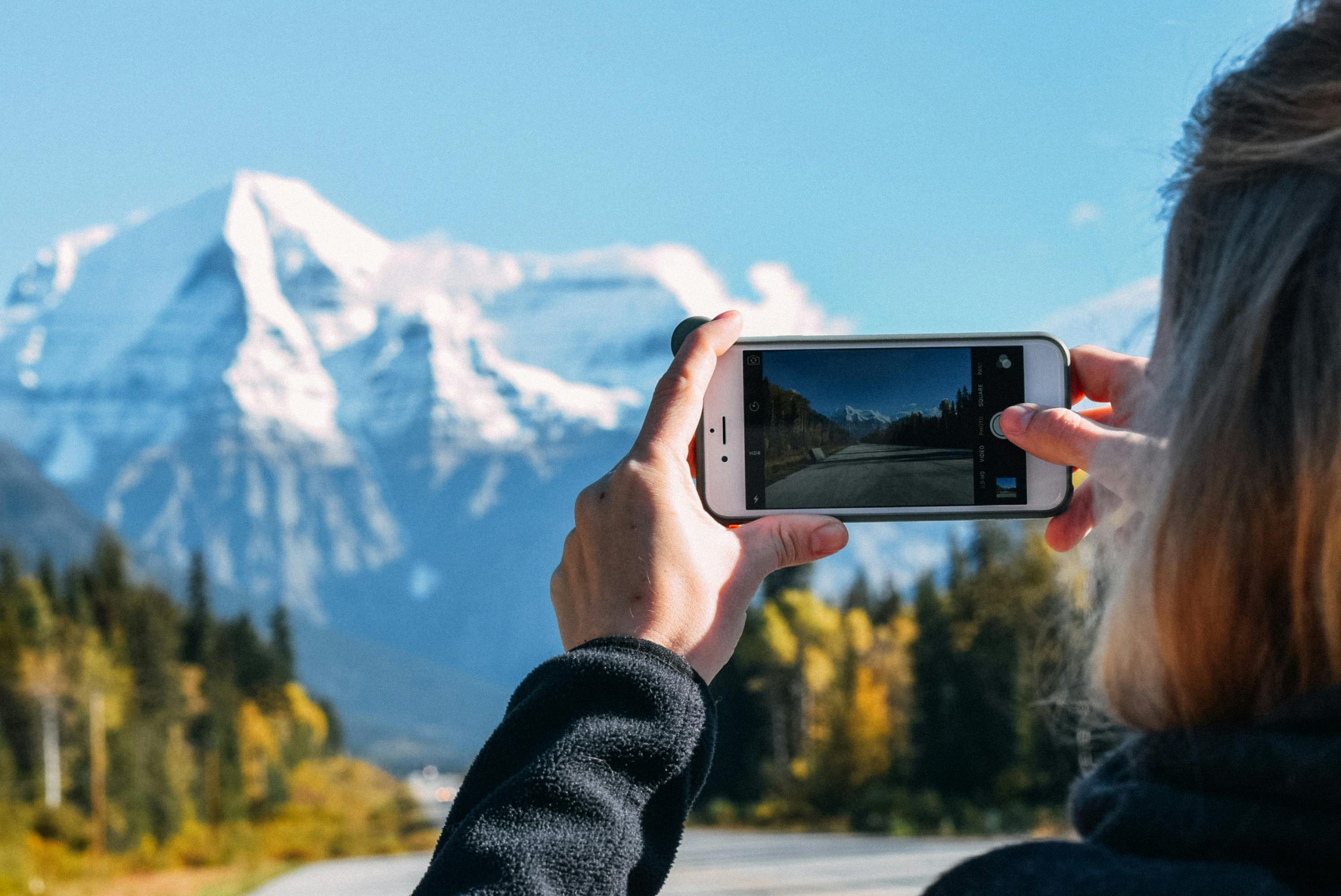 A woman capturing a snowy mountain landscape on a smartphone.