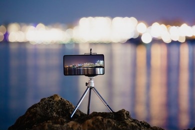 The image shows a smartphone mounted on a small tripod placed on rocks.