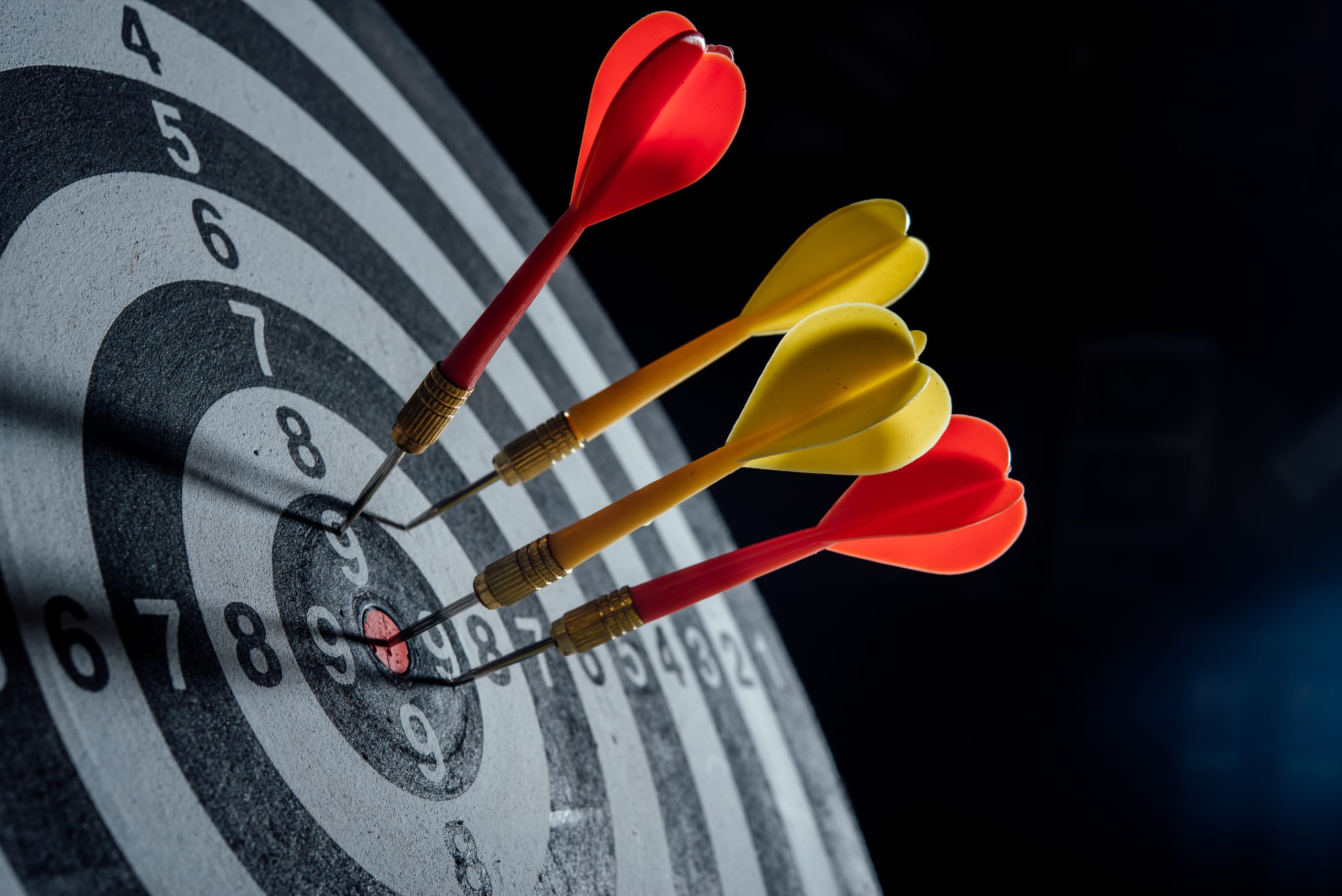 Three darts with red and yellow flights are embedded in the center of a dartboard, with the focus on goal setting. Image by jcompa on Freepik.
