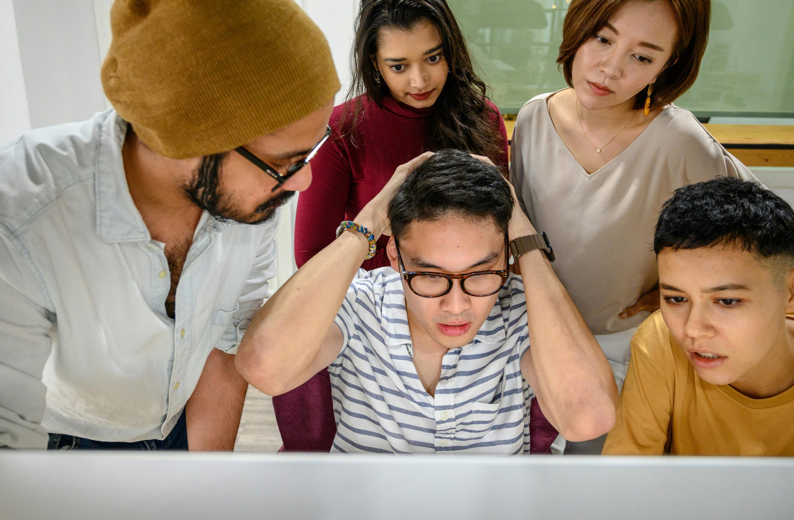Colleagues at work gathered closely around a computer, displaying expressions of concern and focus.